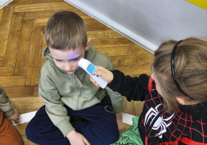 Na zdjęciu widzimy dwóch chłopców. Jeden chłopiec mierzy temperaturę drugiemu za pomocą termometru do ciała.