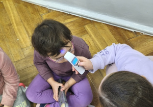 Na zdjęciu widzimy dwie dziewczynki. Jedna dziewczynka mierzy temperaturę drugiej za pomocą termometru do ciała.