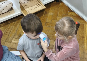 Na zdjęciu widzimy dziewczynkę, która mierzy temperaturę ciała koledze z grupy.