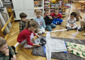 Na zdjęciu widzimy dziewczynkę, która ubiera niewidzialnego Tadka w czapkę.