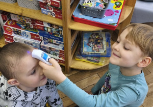 Na zdjęciu widzimy dwóch chłopców. Jeden chłopiec mierzy temperaturę drugiemu za pomocą termometru do ciała.