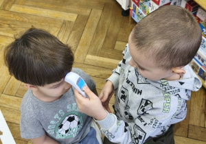 Na zdjęciu widzimy dwóch chłopców. Jeden chłopiec mierzy temperaturę drugiemu za pomocą termometru do ciała.