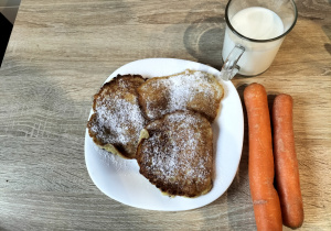 Na zdjęciu widzimy talerz z jabłuszkowymi placuszkami. Obok talerza znajduje się szklanka z mlekiem oraz marchewki dla Rudolfa.