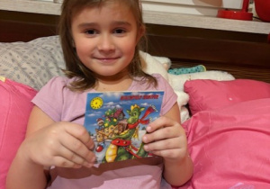 Na zdjęciu widzimy dziewczynkę, która trzyma w ręku świateczną kwiążeczkę.