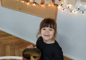 Dziewczynka siedzi na krześle z pudełkiem ciasteczek na kolanach.