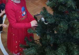 Dziewczynka zawiesza ozdobę na choince.