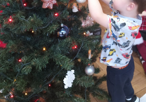 Chłopiec zawiesza ozdobę na choince.