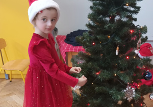 Dziewczynka zawiesza ozdobę na choince.