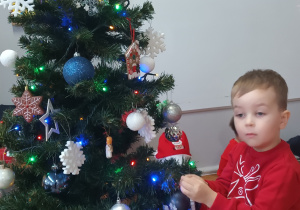 Chłopiec zawiesza ozdobę na choince.