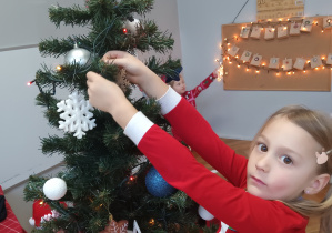 Dziewczynka zawiesza ozdobę na choince.