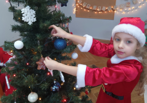 Dziewczynka zawiesza ozdobę na choince.