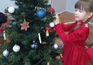 Dziewczynka zawiesza ozdobę na choince.