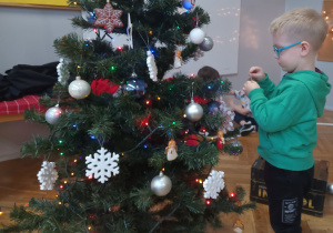 Chłopiec zawiesza ozdobę na choince.