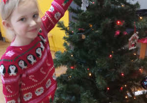 Dziewczynka zawiesza ozdobę na choince.