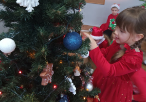Dziewczynka zawiesza ozdobę na choince.