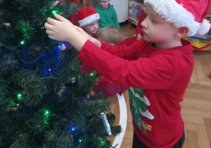 Chłopiec zawiesza ozdobę na choince.