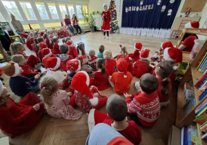 kobieta w stroju Mikołajki, stoi przed dziećmi. W tle widać napis mikołajki