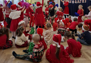 dzieci w czerwonych strojach machją kolorowymi pomponami