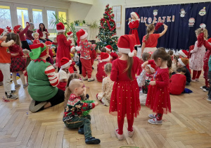 grupa dzieci w czerwonych strojach patrzy na kobietę w stroju Mikołajki