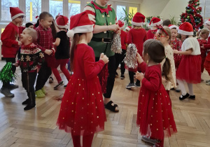 kobieta w stoju elfa stoi przed dziwczynkami które są w czerwonych sukienkach