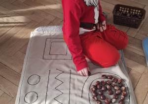 dziecko układa kasztany na wyszytym wzorze