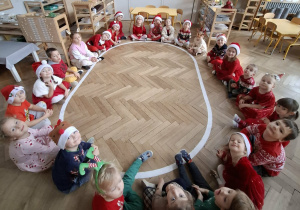dzieci siedzą na elipsie w strojach z elementami świątecznymi