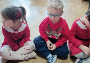 Dzieci siedzą na podłodze w siadzie skrzyżnym.