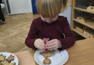 Na zdjęciu widzimy dziewczynkę, która dekoruje pisakami i posypkami pierniczki.