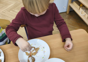 Na zdjęciu widzimy dziewczynkę, która dekoruje posypkami pierniczki.