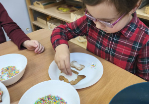 Na zdjęciu widzimy dziewczynkę, która dekoruje posypkami pierniczki.