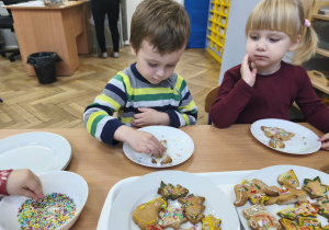 Na zdjęciu widzimy dwójkę dzieci, które dekorują posypkami pierniczki.