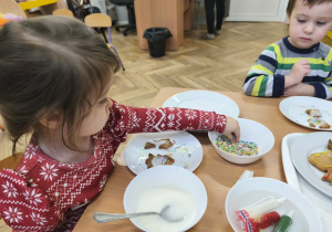 Na zdjęciu widzimy dziewczynkę, która dekoruje kolorową posypką pierniczki.