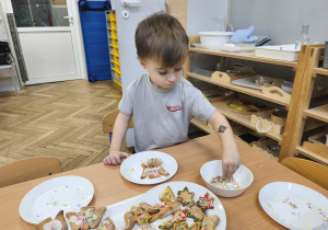 Na zdjęciu widzimy chłopca, który dekoruje kolorową posypką pierniczki.