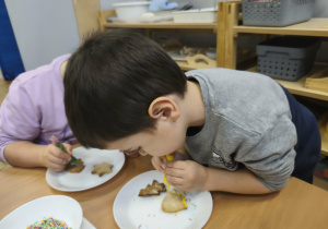 Na zdjęciu widzimy chłopca, który dekoruje pisakami i posypkami pierniczki.