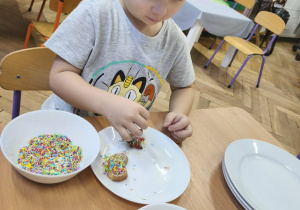 Na zdjęciu widzimy chłopca, który dekoruje pisakami i posypkami pierniczki.