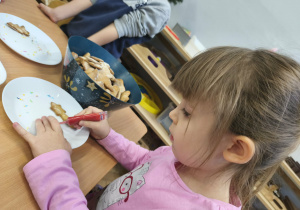 Na zdjęciu widzimy dziewczynkę, która dekoruje pisakami i posypkami pierniczki.