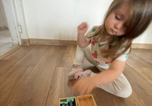 Na zdjęciu widzimy dziewczynkę, która sprząta swoje gumki i spinki do pudełka.