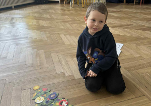 Zdjęcie przedstawia chłopca siedzącego na podłodze, obok puzzli choinki.