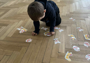 Zdjęcie przedstawia chłopca układającego obrazki na podłodze.