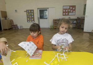 Zdjęcie przedstawia dzieci wycinające obrazki przy stoliku.
