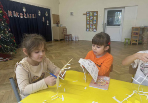 Zdjęcie przedstawia dzieci wycinające obrazki przy stoliku.
