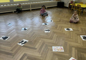 Zdjęcie przedstawia dzieci siedzące na podłodze. Przed nimi rozsypane są obrazki.