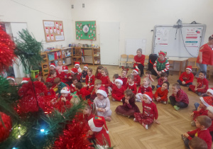 dzieci siedzą na podłodze i słuchają zadania od Mikołaja