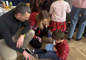 Zdjęcie przedstawia chłopca oglądającego swój prezent, wspólnie z rodzicami.