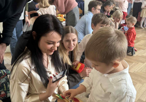Zdjęcie przedstawia chłopca oglądającego swój prezent razem z rodzicami.