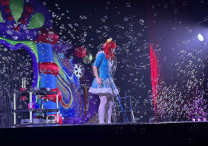 Zdjęcie przedstawia aktorkę stojącą na scenie, wśród baniek.