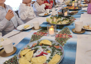 Dzieci siedzą za wspólnym stołem i jedzą potrawy Wigilijne