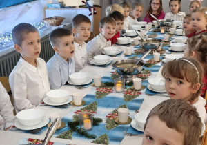 Dzieci siedzą za wspólnym stołem i jedzą potrawy Wigilijne