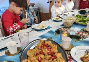 Dzieci siedzą za wspólnym stołem i jedzą potrawy Wigilijne