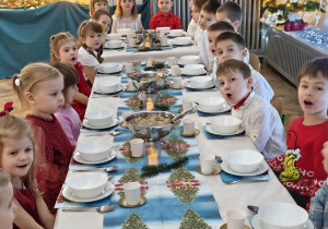 Dzieci siedzą za wspólnym stołem i jedzą potrawy Wigilijne